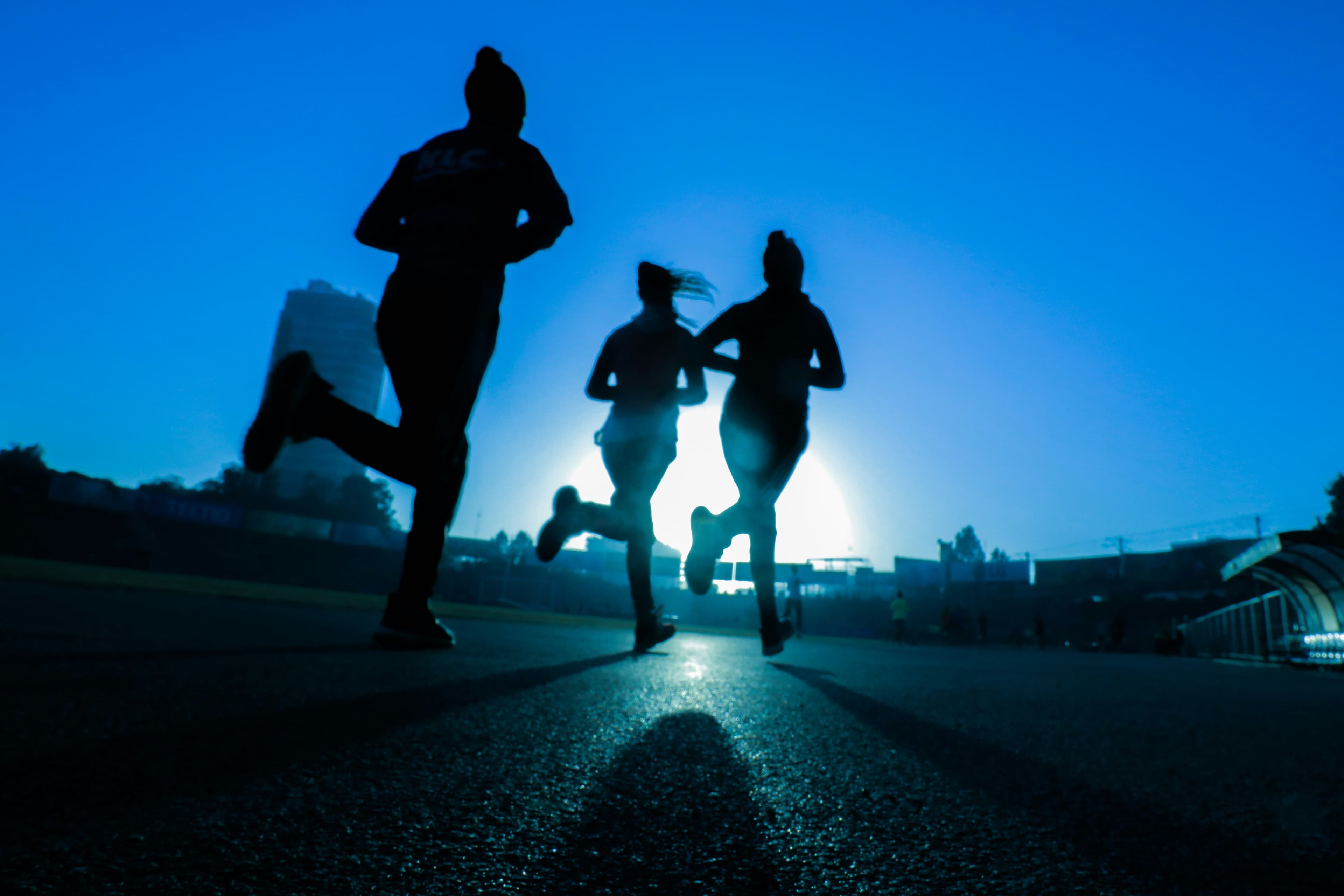 Siluetas de tres corredores al atardecer en una pista
