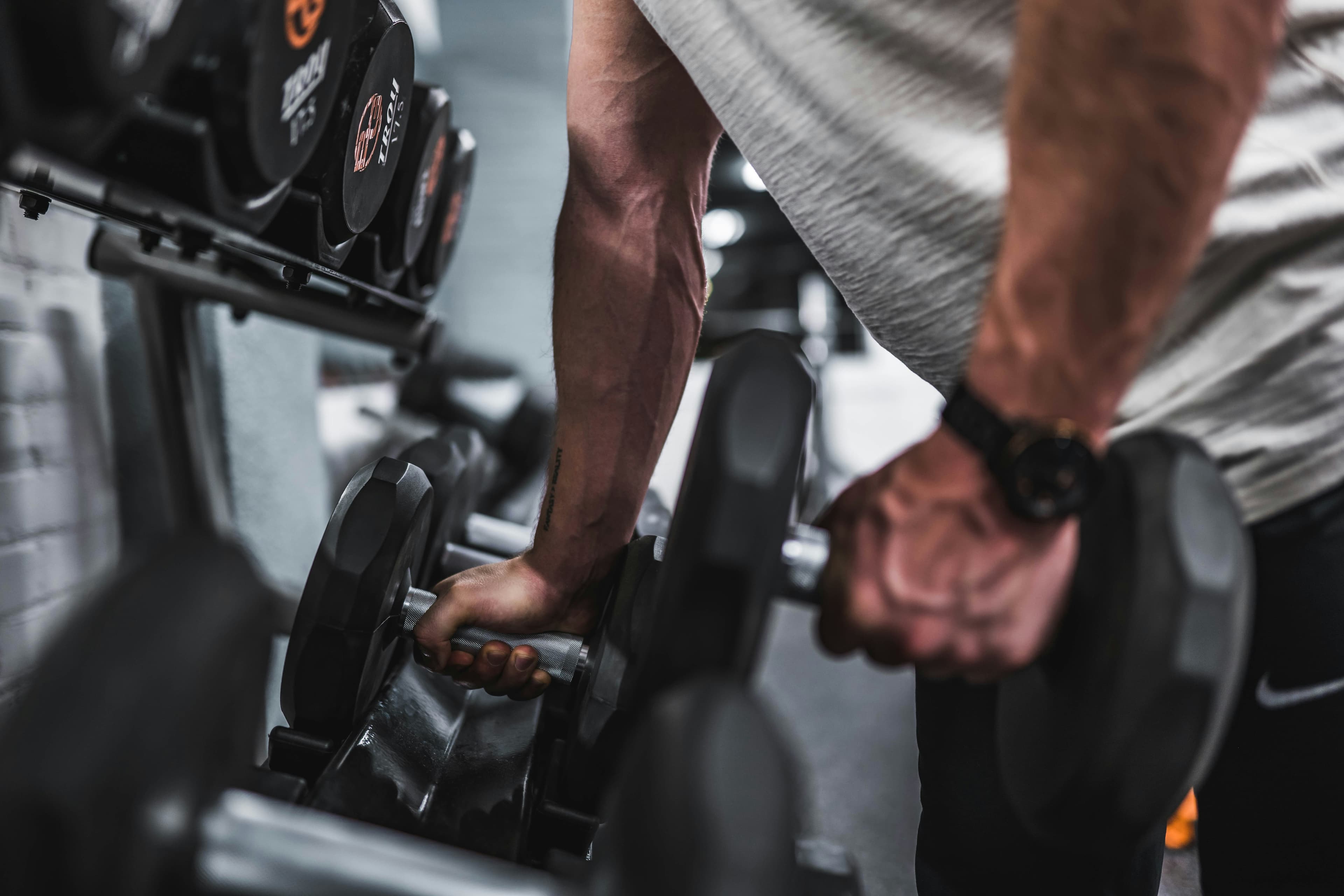 Manos cogiendo mancuernas de un rack en un gimnasio